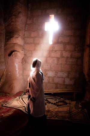 Light beam through a cross-shaped window illuminating a veiled woman